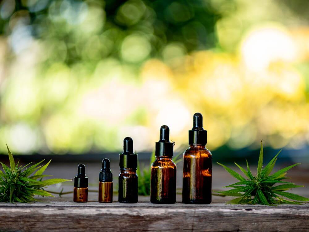 5 bottles of cbd oil in various sizes. surrounding by cannabis leaves